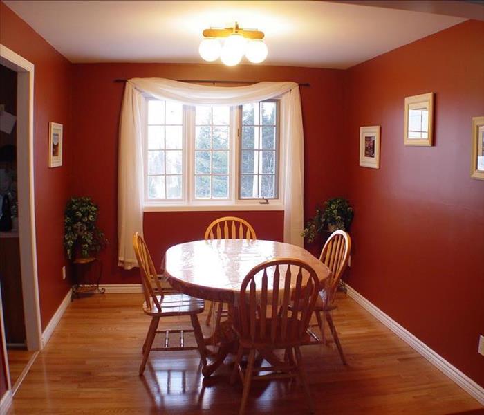 The same room after renovations with deep red painted walls, light wood dining table and chairs, and a white drapery